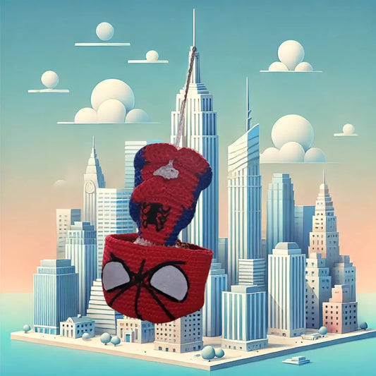 A Spiderman-inspired amigurumi, crocheted with red and blue details, hanging from a thread against a stylized background of a city with skyscrapers and clouds.